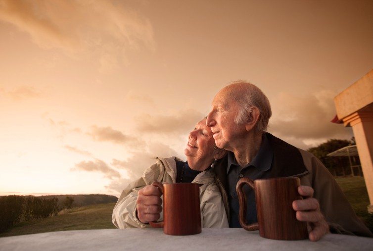 old couple holding mugs, outside at sunset
